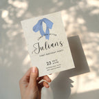 Minimalist first birthday invitation with blue bow illustration and soft neutral background