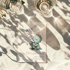 Dinosaur first birthday invitation with cute baby dinosaur holding a gift in soft pastel colors