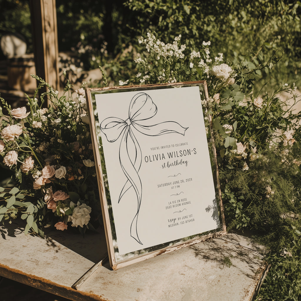 Minimalist black bow first birthday invitation with a hand-drawn ribbon, elegant black typography, and a clean white monochrome layout.