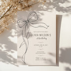 Minimalist black bow first birthday invitation with a hand-drawn ribbon, elegant black typography, and a clean white monochrome layout.