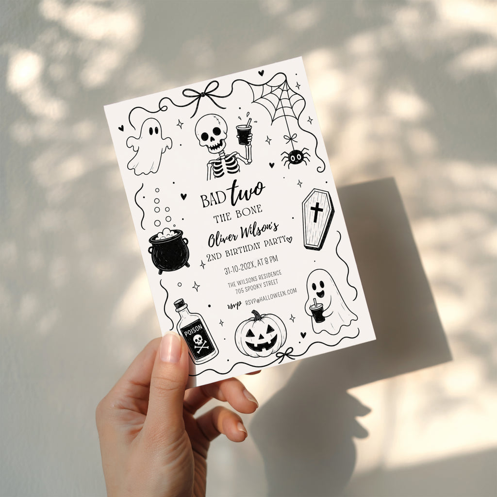 Bad Two the Bone birthday invitation for a second birthday with black and white skeleton, ghost, cauldron, coffin, spider and pumpkin illustrations.