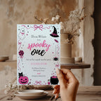 Spooky One first birthday girl invitation in pink and black with cute ghost, witch hat, spider, lollipop, pink pumpkin and bubbling Halloween cauldron illustrations.
