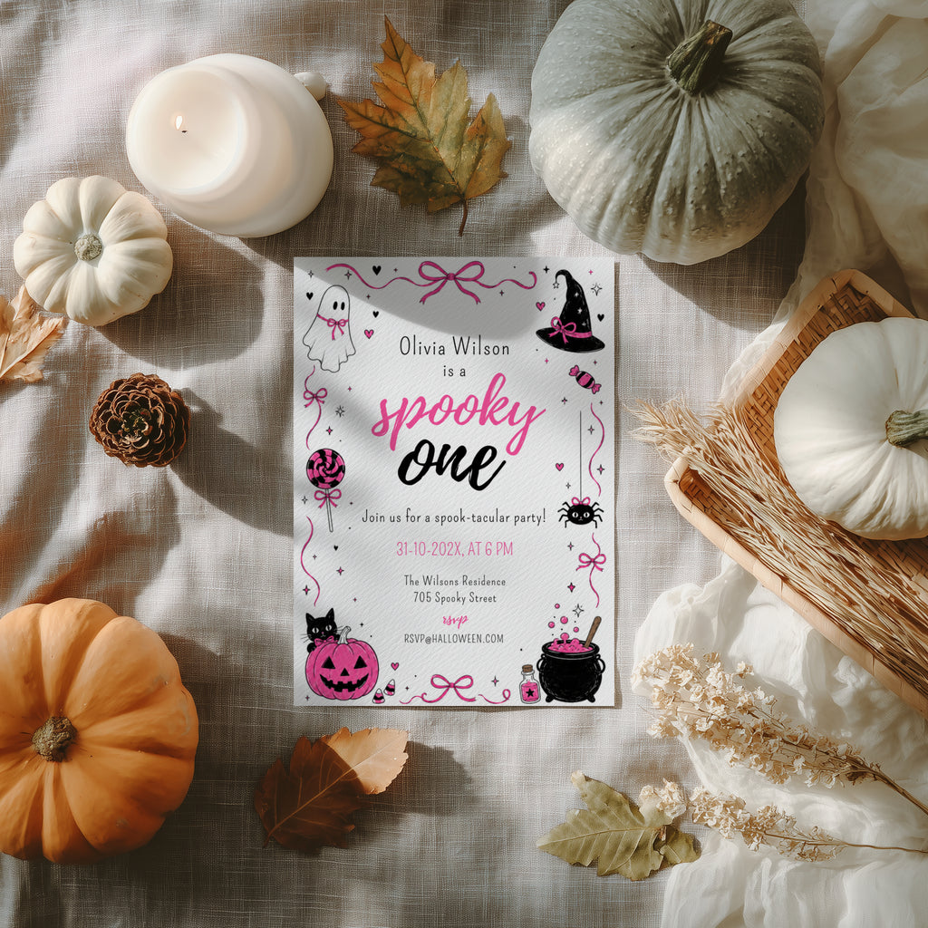 Spooky One first birthday girl invitation in pink and black with cute ghost, witch hat, spider, lollipop, pink pumpkin and bubbling Halloween cauldron illustrations.