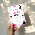 Spooky One first birthday girl invitation in pink and black with cute ghost, witch hat, spider, lollipop, pink pumpkin and bubbling Halloween cauldron illustrations.