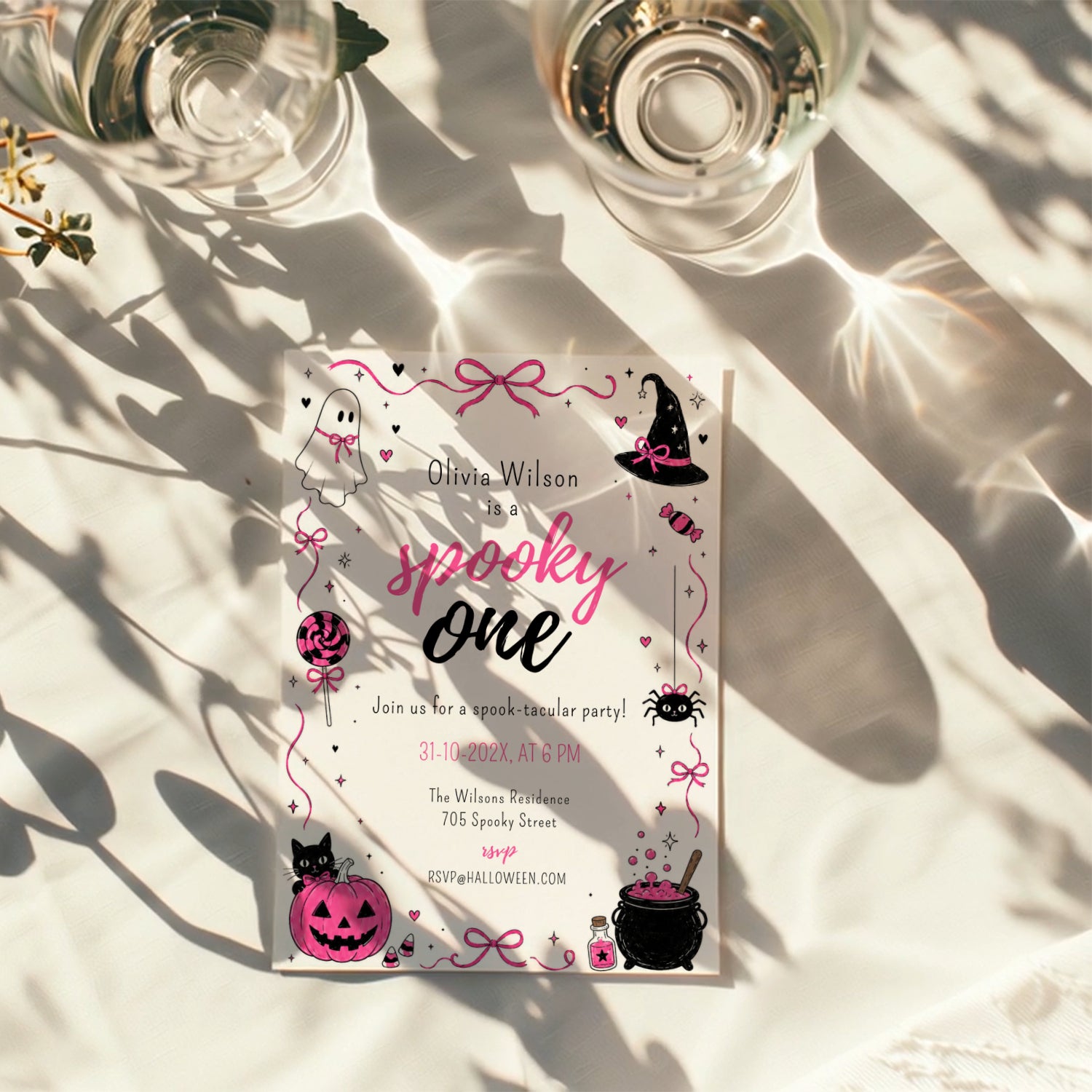 Spooky One first birthday girl invitation in pink and black with cute ghost, witch hat, spider, lollipop, pink pumpkin and bubbling Halloween cauldron illustrations.